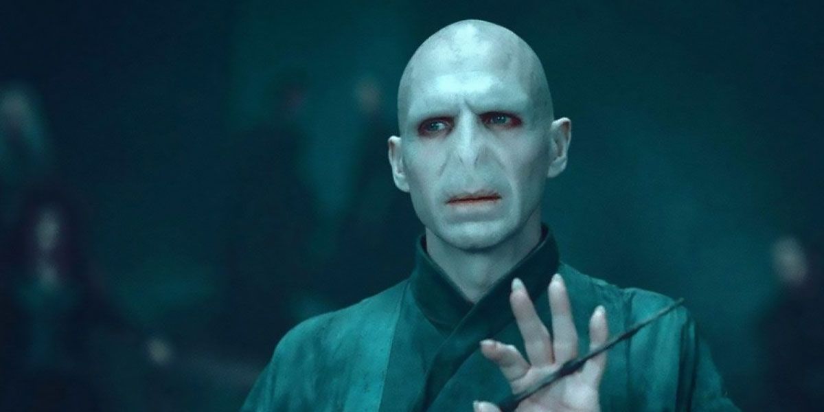 Voldemort In Harry Potter holds up his hand while brandishing a wand