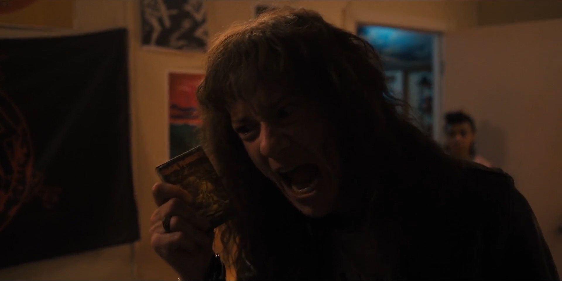 Eddie Munson holding a cassette tape a screaming in Stranger Things 4