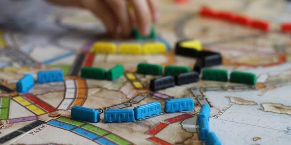 The board for Ticket to Ride, mid-game, with a hand placing a piece in the background