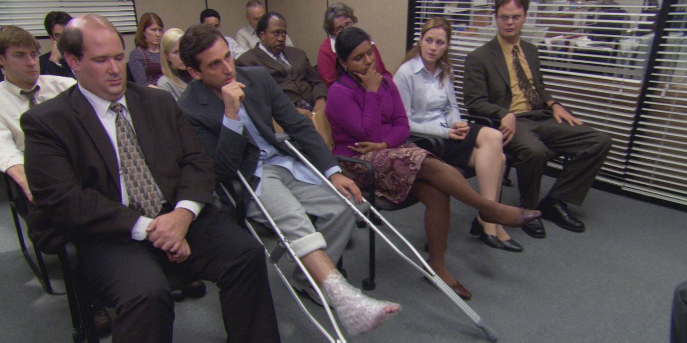 A equipe do The Office está sentada na sala de conferências, com Michael segurando muletas