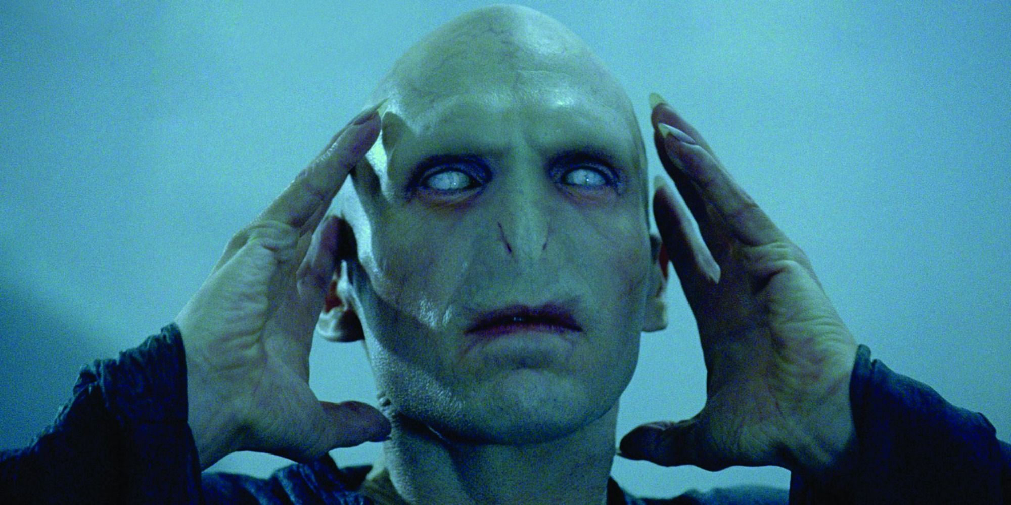 Voldemort with white eyes, holds his hands up to the sides of his head