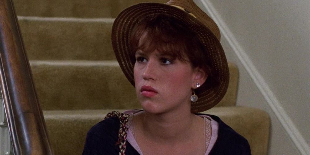 Sam sits on the stairs with her hat on her head in Sixteen Candles.