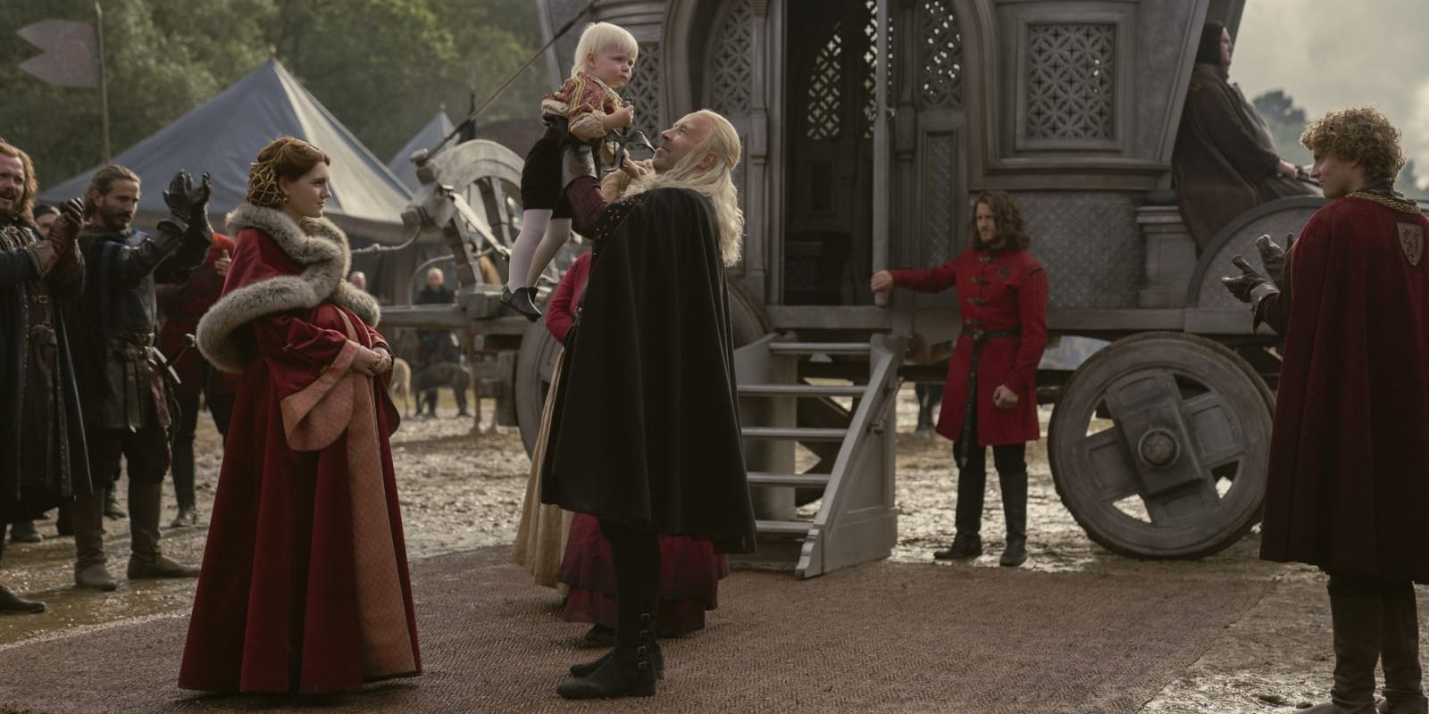 King Viserys I holds up a young Aegon Targaryen while Alicent Hightowe watches in House of the Dragon