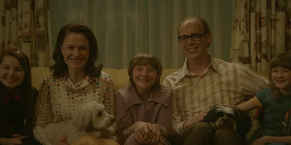 A family sitting on the couch with their dog smiling in A Friend of the Family.