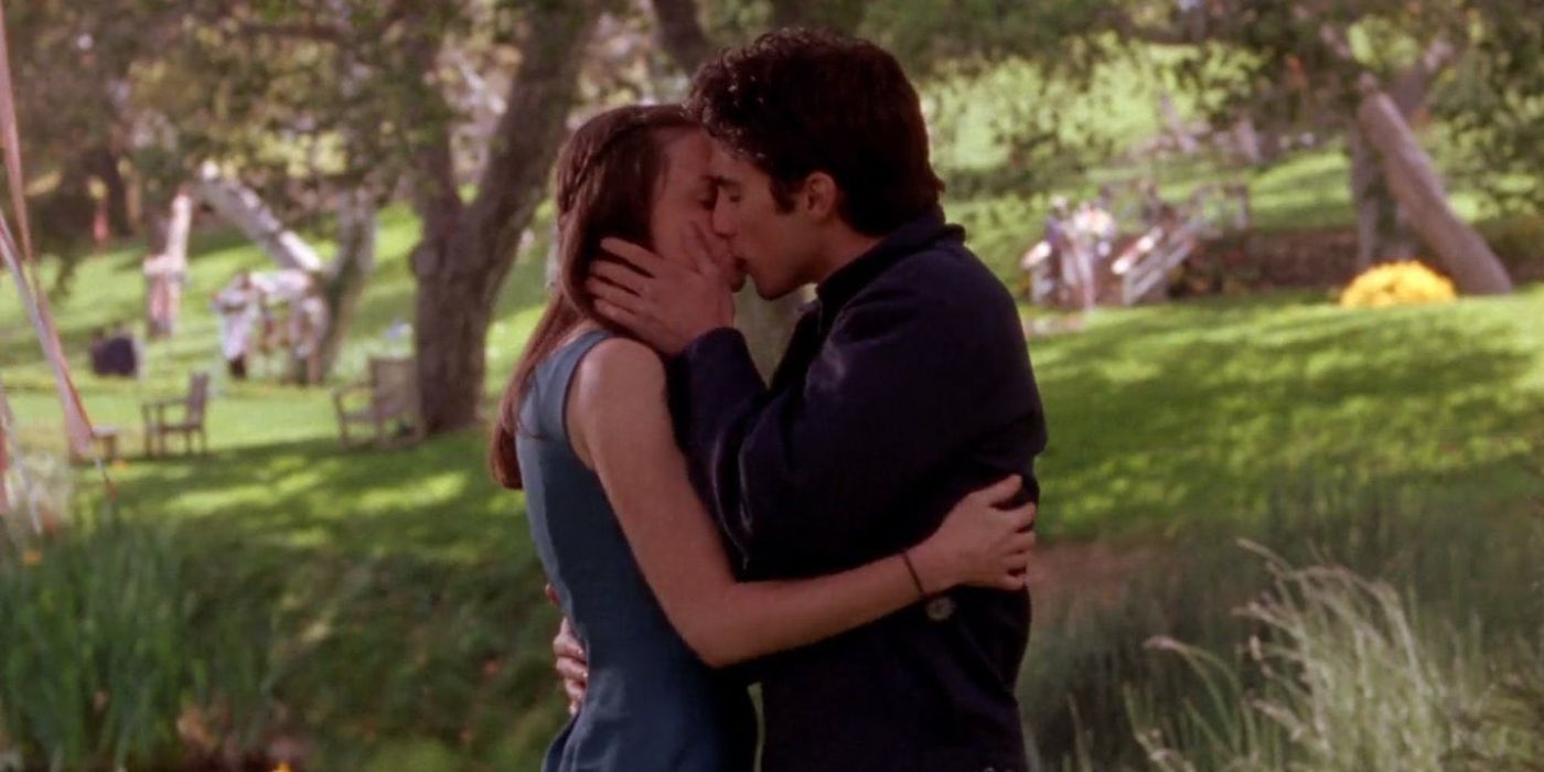 Gilmore Girls Rory and Jess First Kiss in a grassy, tree-lined area.