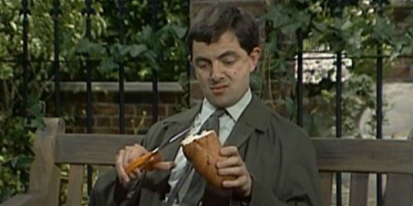 Mr. Bean cutting his bread with scissors on a bench