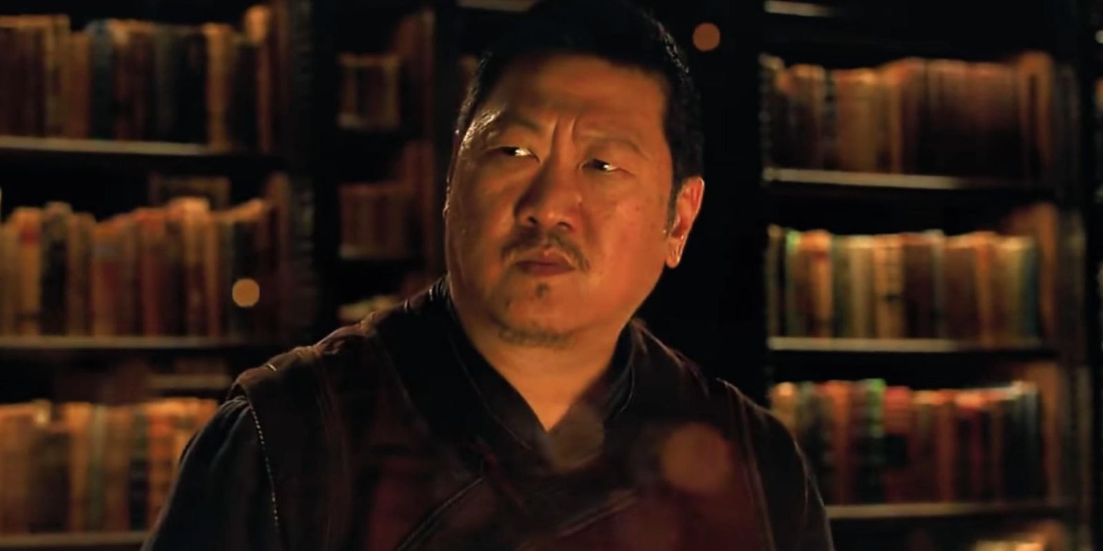 benedict wong as wong from the marvel cinematic universe in front of several book shelves