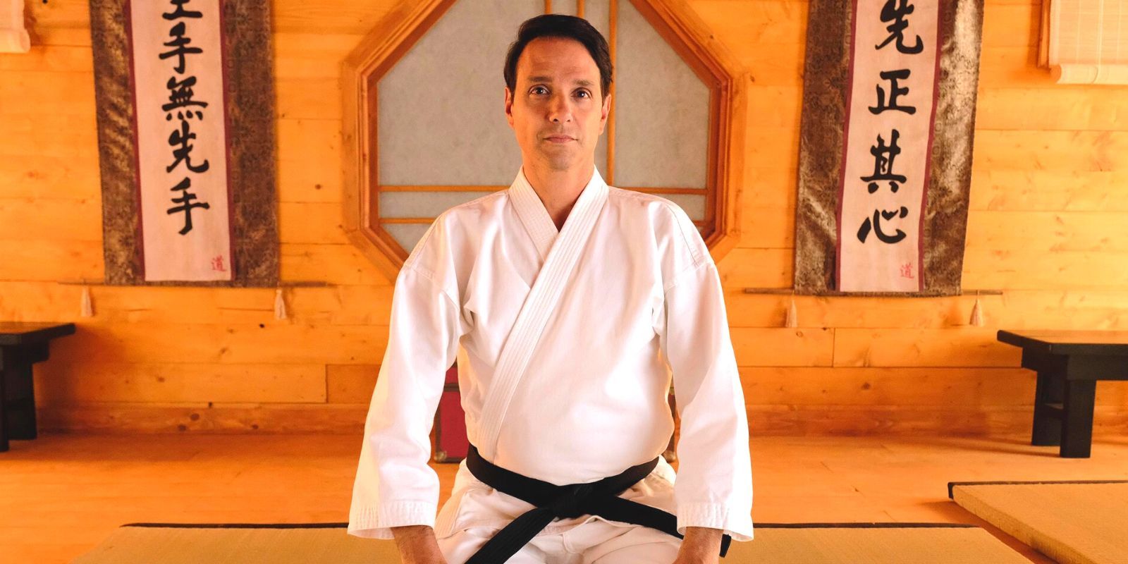 Ralph Macchio in full karate gi kneeling in a dojo in Cobra Kai