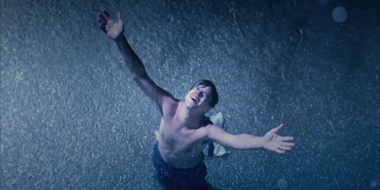 Shirtless man raises his hands in the rain