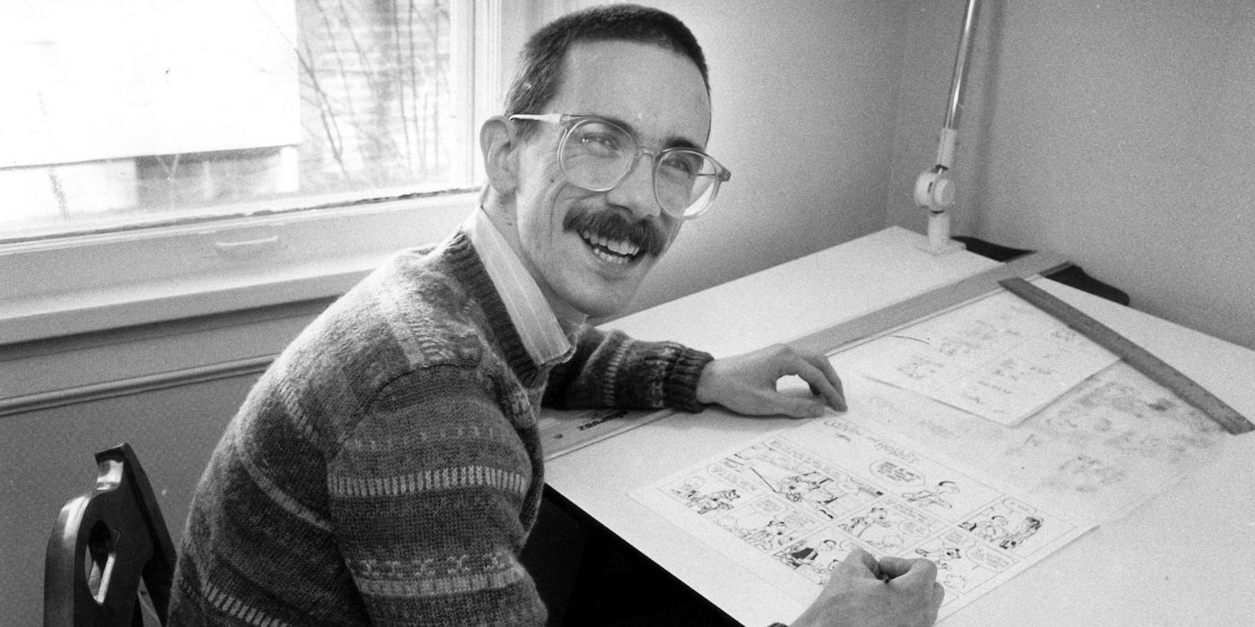 Bill Watterson smiles while leaning over a drawing board