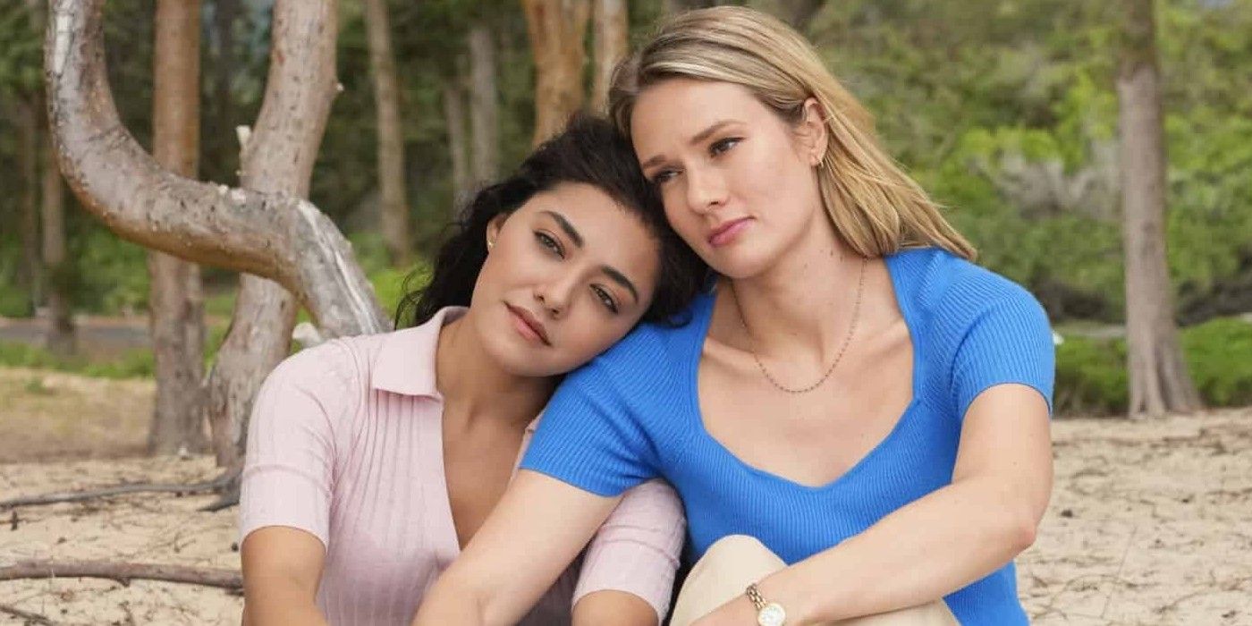 NCIS: Hawai'i Lucy (interpretada por Yasmine Al-Bustami) senta-se com a cabeça no ombro de Kate (interpretada por Tori Anderson) na praia