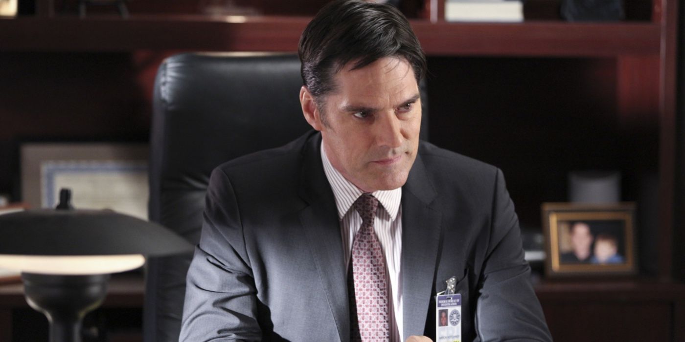 Hotch sitting at his desk looking frustrated with a blurred out photo of his son in the background