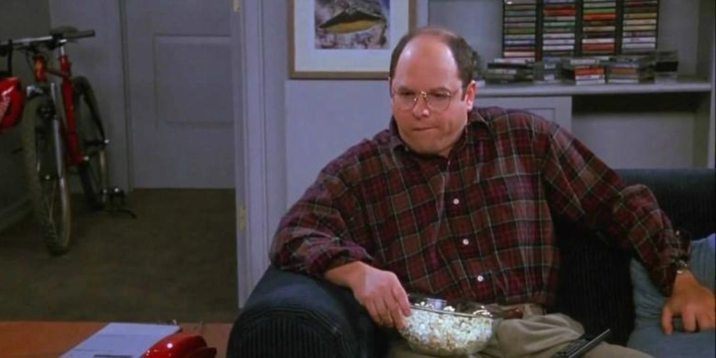 George sentado en una silla con un bol de palomitas de maíz en Seinfeld