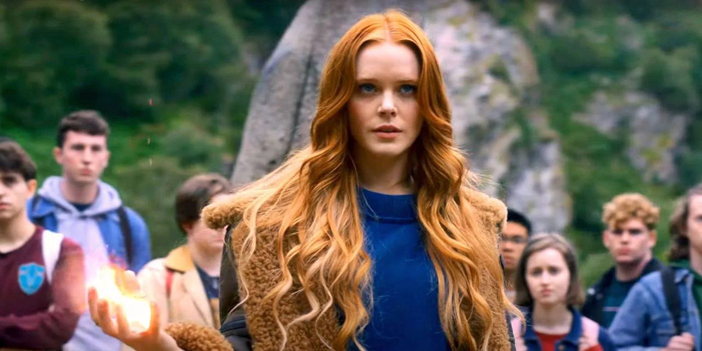 Bloom holding a fireball in her hand with people behind her in Fate: The Winx Saga.