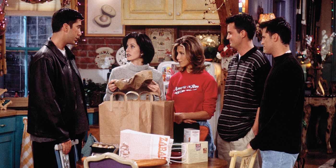 The cast of Friends standing in the kitchen with shopping bags.
