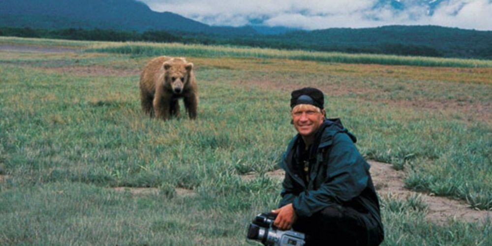 Treadwell is in a field with a grizzly bear behind him in the documentary Grizzly Man