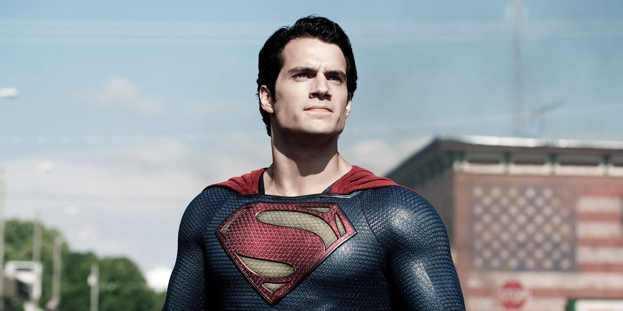 Henry Cavill standing in front of an American flag as Superman in Man of Steel.