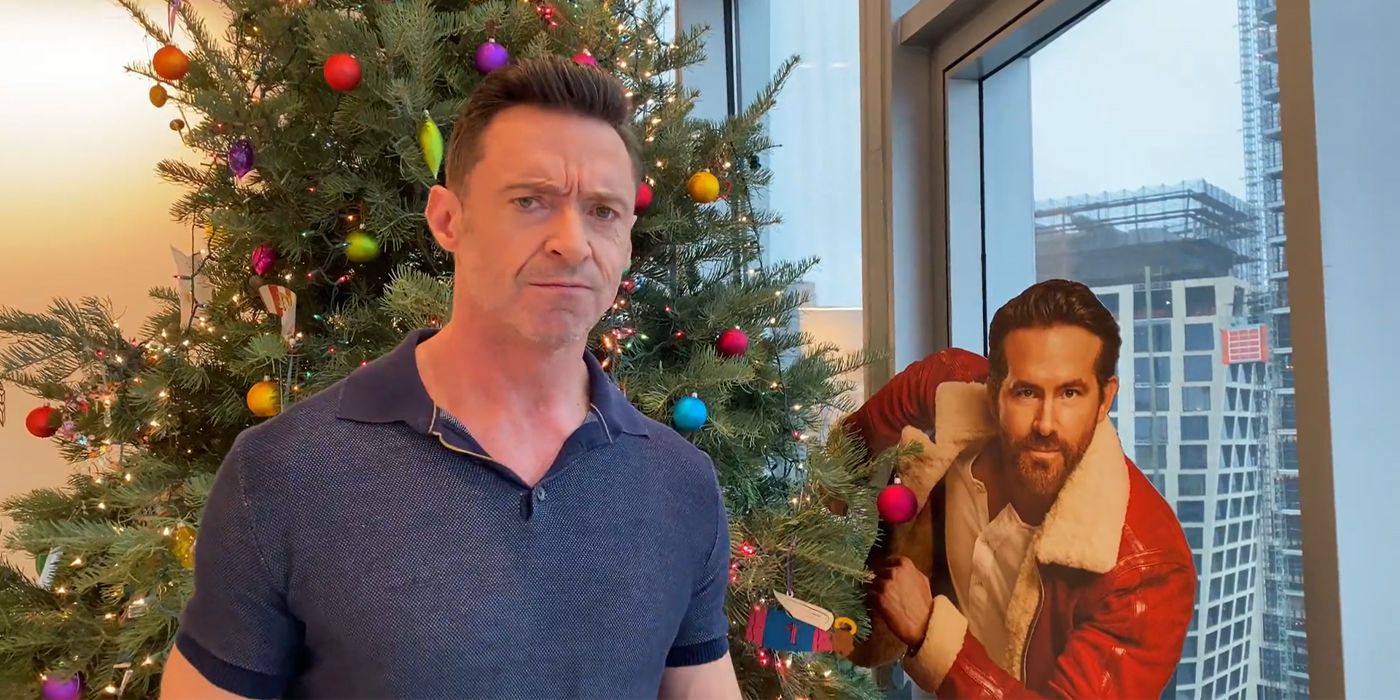 Actor Hugh Jackman stands beside a Christmas tree and standee of Ryan Reynolds as he appears in the movie Spirited