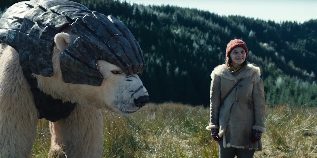 Lyra sorri ao lado do urso polar blindado Iorek perto de uma floresta em His Dark Materials