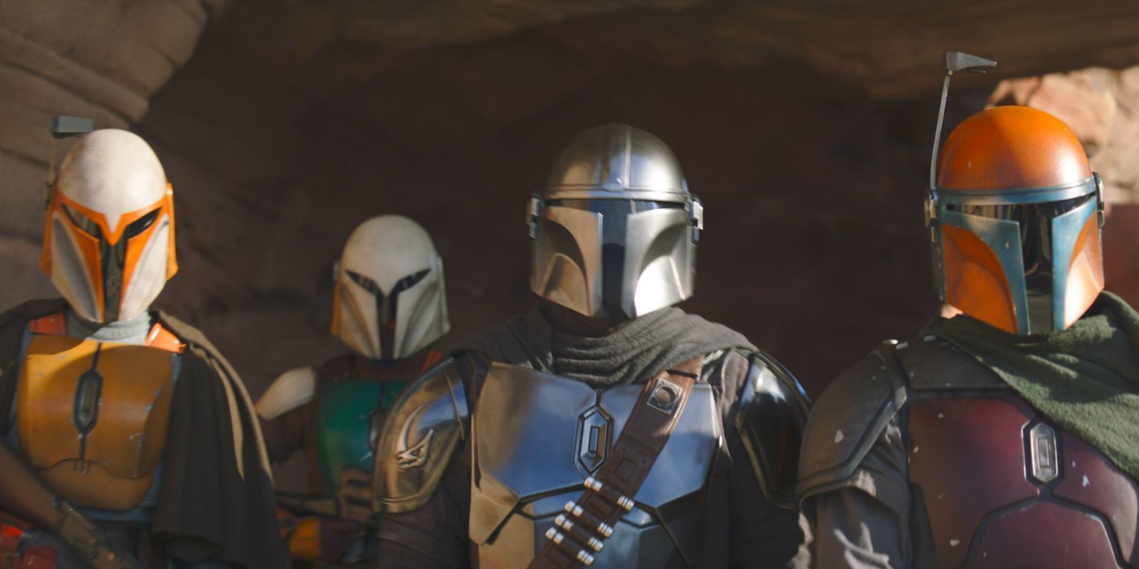 A group of Mandalorians in armor standing in a rock cave 