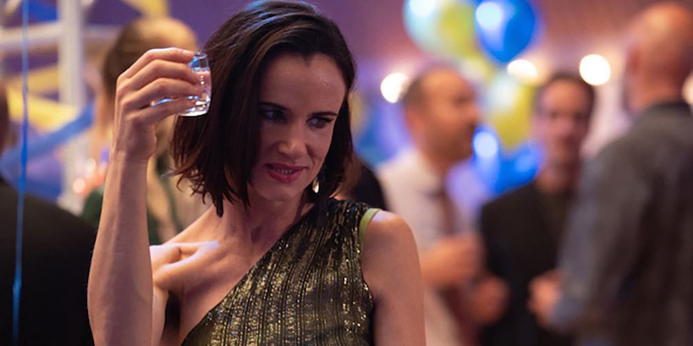 Adult Natalie from Yellowjackets in a dress at a party, raising a glass.