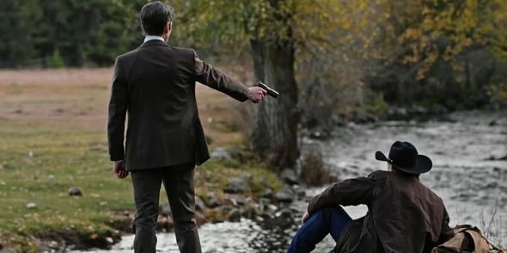 Yellowstone's Jamie Dutton pointing a gun at Garrett Randall, who is sitting down by a river