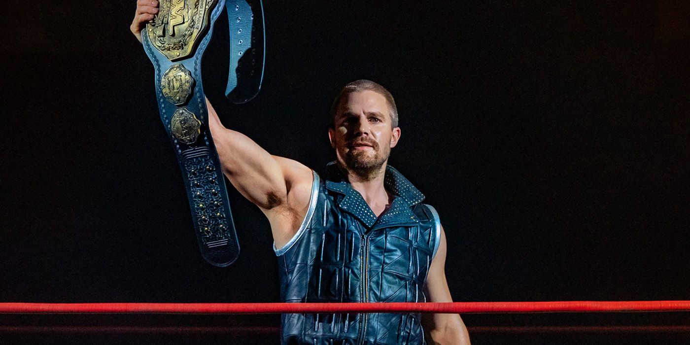 Heels's Stephen Amell as Jack Spade in the ring holding up a title belt.