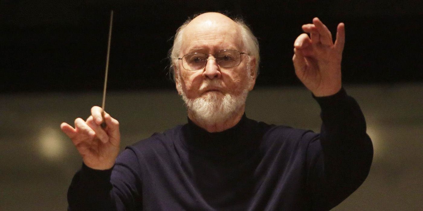 John Williams in the middle of conducting, waving a baton with his right hand.