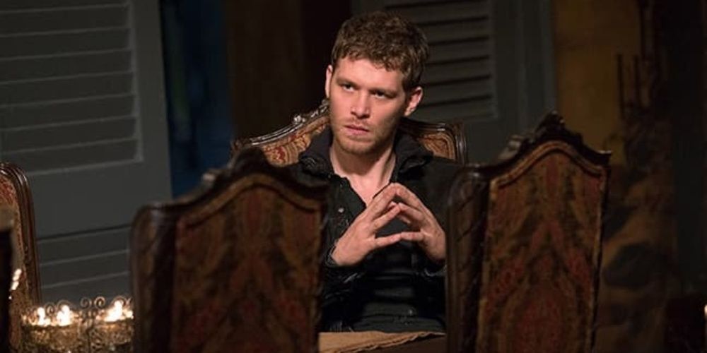 Klaus sits on a chair at dinner in The Originals. 