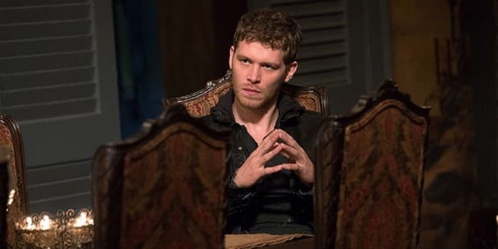 Klaus senta em uma cadeira durante o jantar em The Originals. 