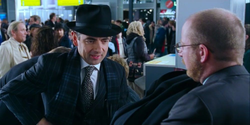 Rowan Atkinson's Love Actually character hands a jacket to airport check-in
