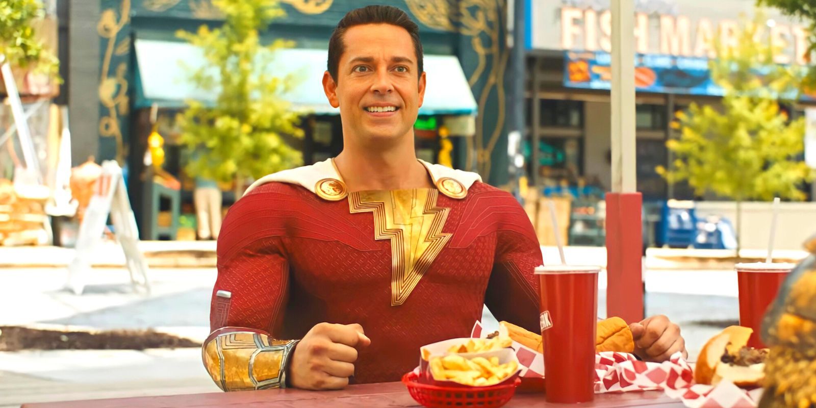 Shazam sitting at the table of a fast food restaurant looking excited