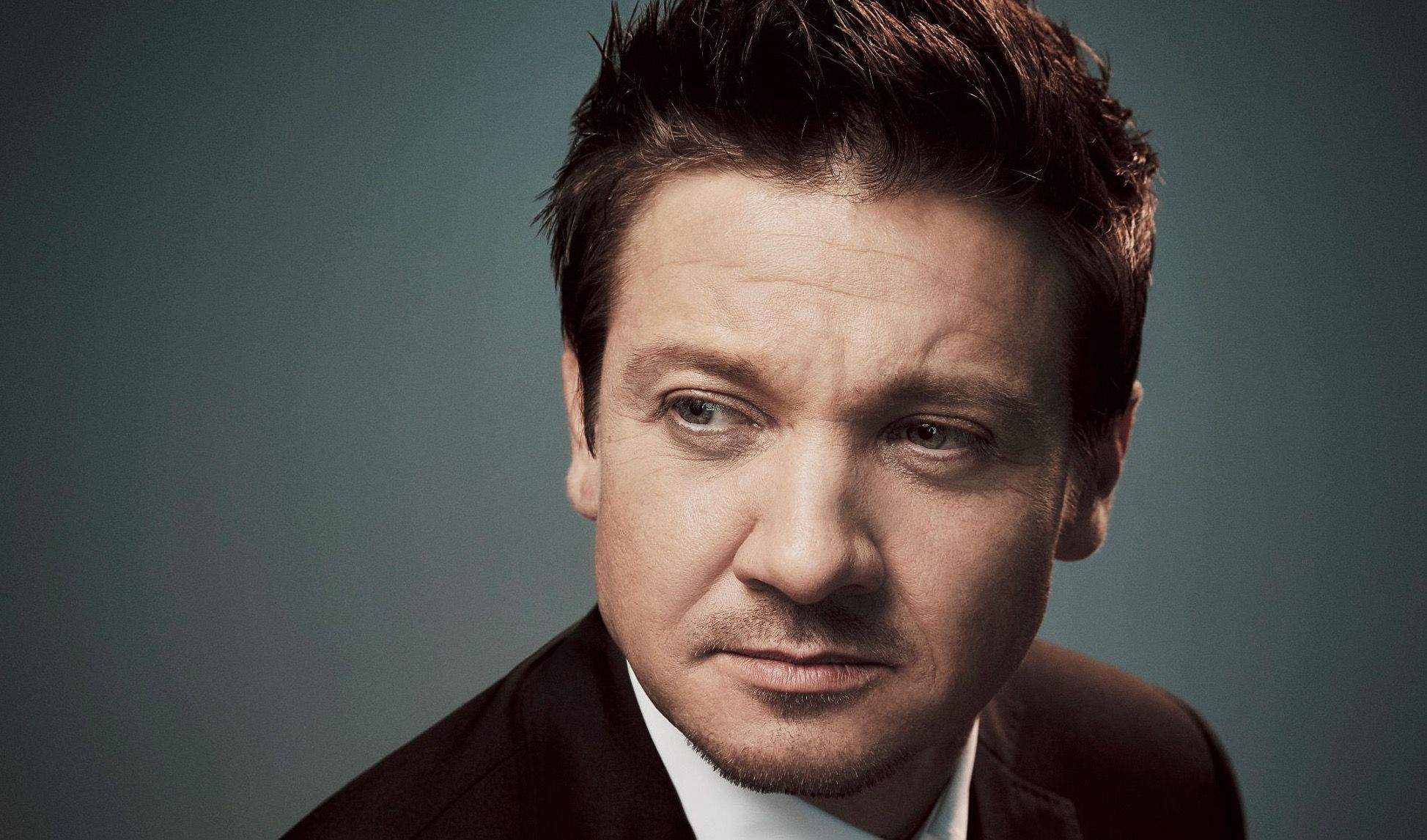 A photo of Jeremy Renner against a gray background.