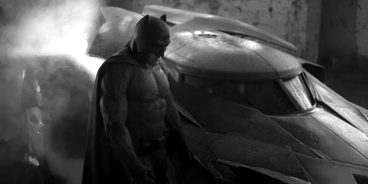 Ben Affleck dressed as Batman, standing beside his heavily armored car.