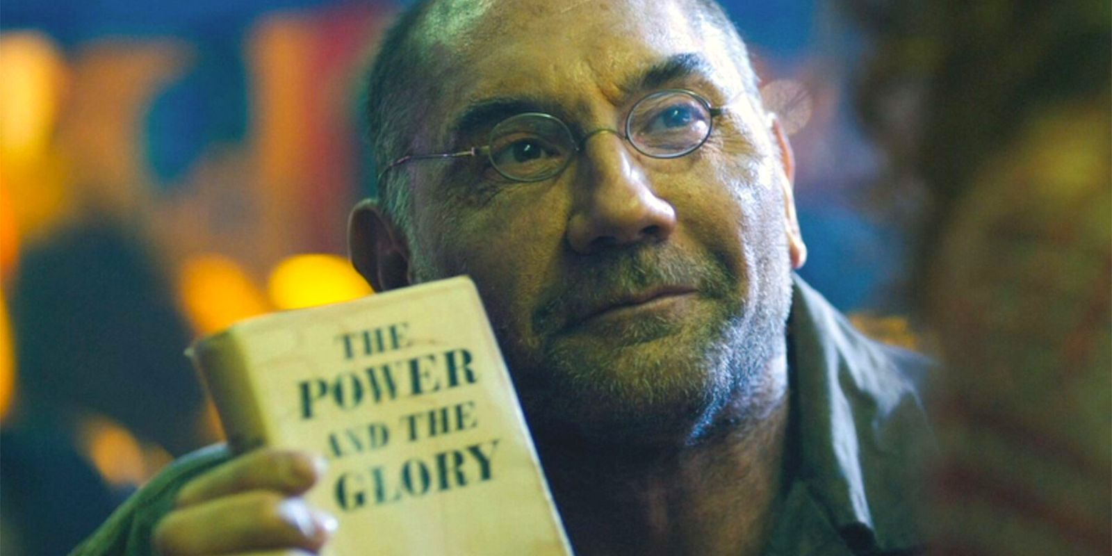 Dave Bautista in spectacles holding up a copy of the book The Power and The Glory