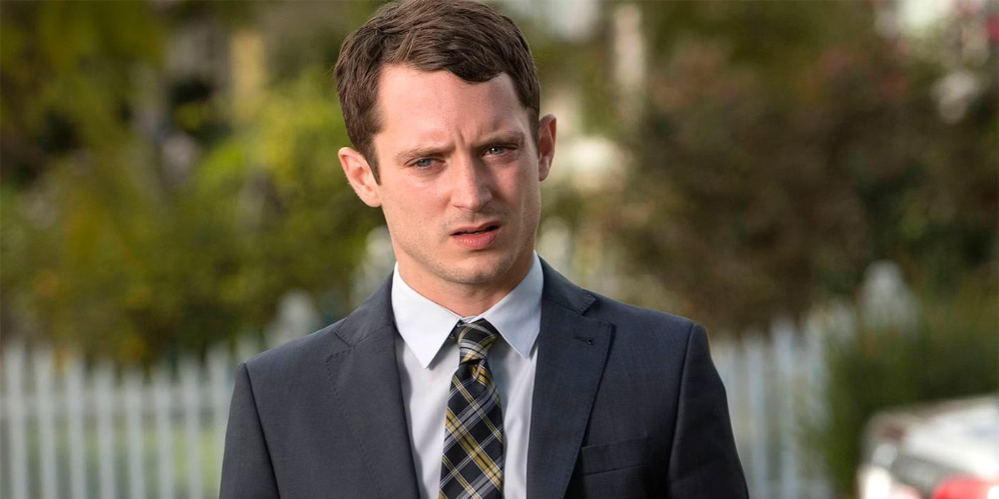 Elijah Wood in a suit and tie outside looking disgusted