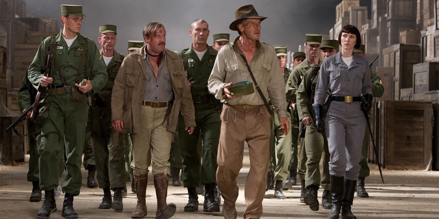 A group of soldiers in green uniforms follow Indiana Jones through a warehouse
