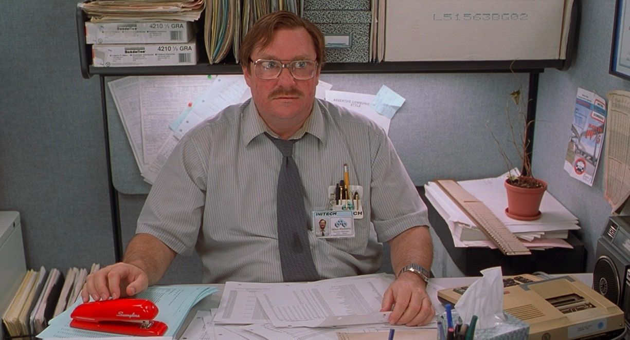 Milton sitting at his office desk with his iconic red stapler