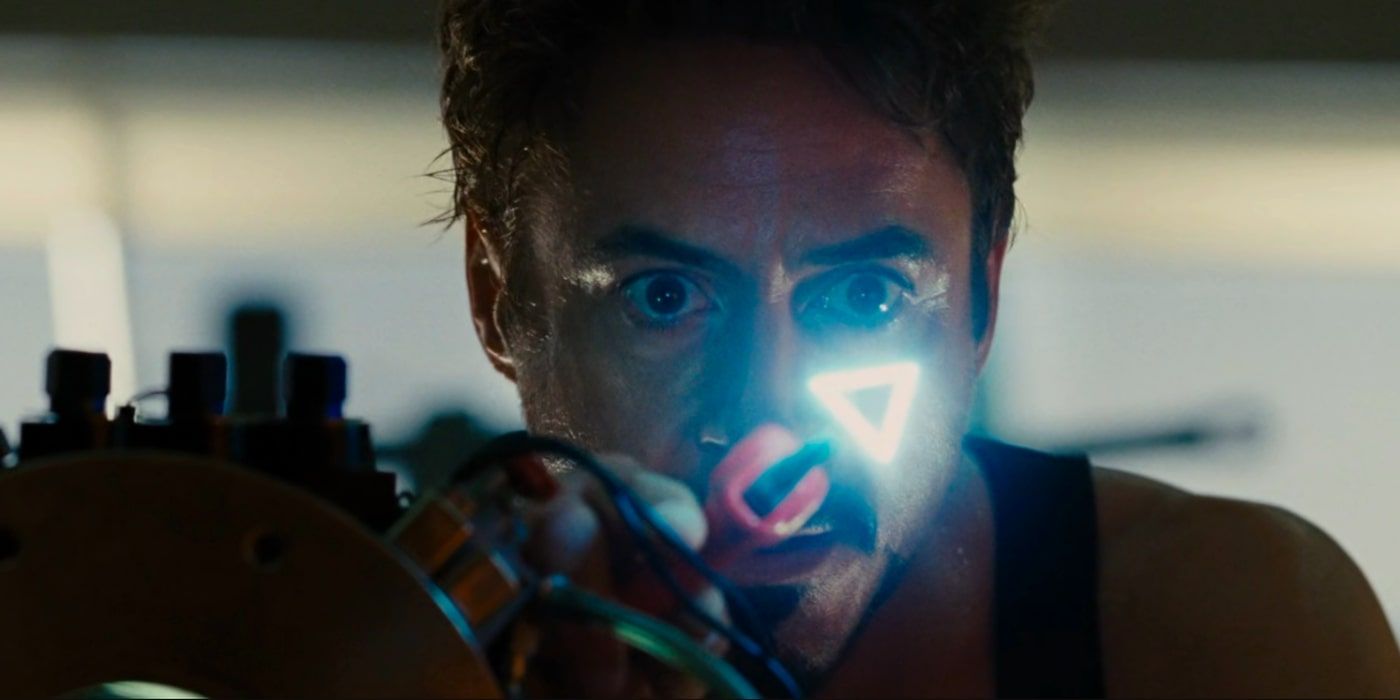 Tony Stark looks in awe at the glowing triangle-shaped element he has created 