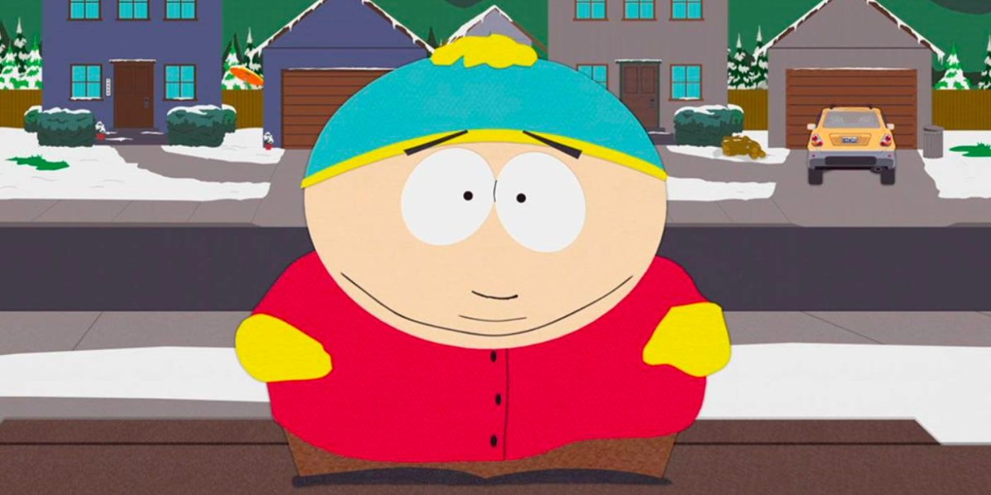 A smiling Eric Cartman stands on a snowy pavement with some houses behind him
