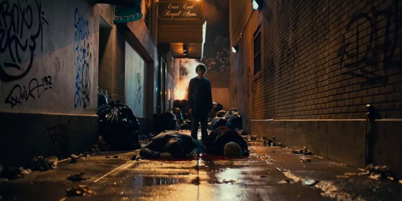 A young Bruce Wayne stands by his parents' bodies, which lay in an alleyway