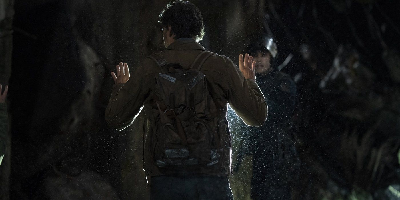 Joel, played by Pedro Pascal, with his hands up as a FEDRA officer points a gun at him from "When You're Lost In The Darkness" from The Last Of Us