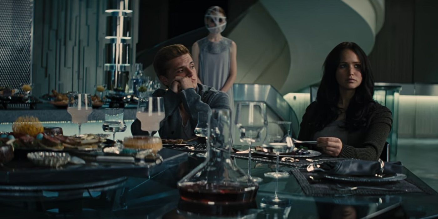 Katniss and Peeta sitting at a table with an Avox in the background in Hunger Games Catching Fire