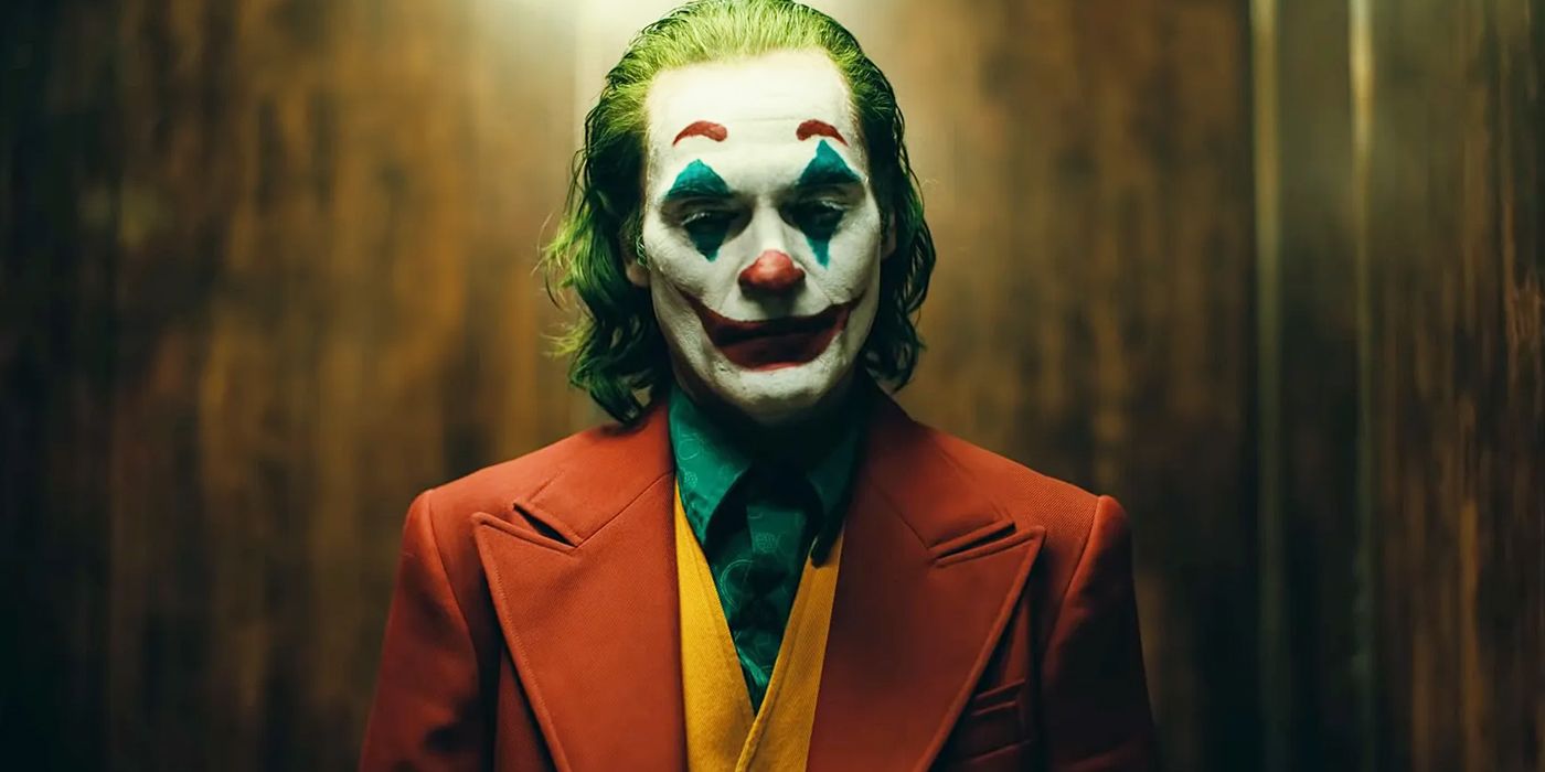Arthur Fleck (Joaquin Phoenix) smiles in clown makeup while riding an elevator in Todd Phillips' Joker (2019).
