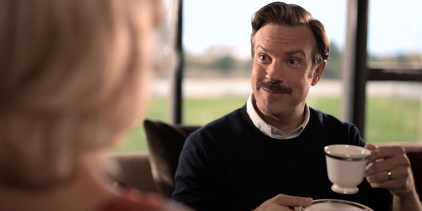 Ted holding a cup of tea and smiling in a scene from Ted Lasso.