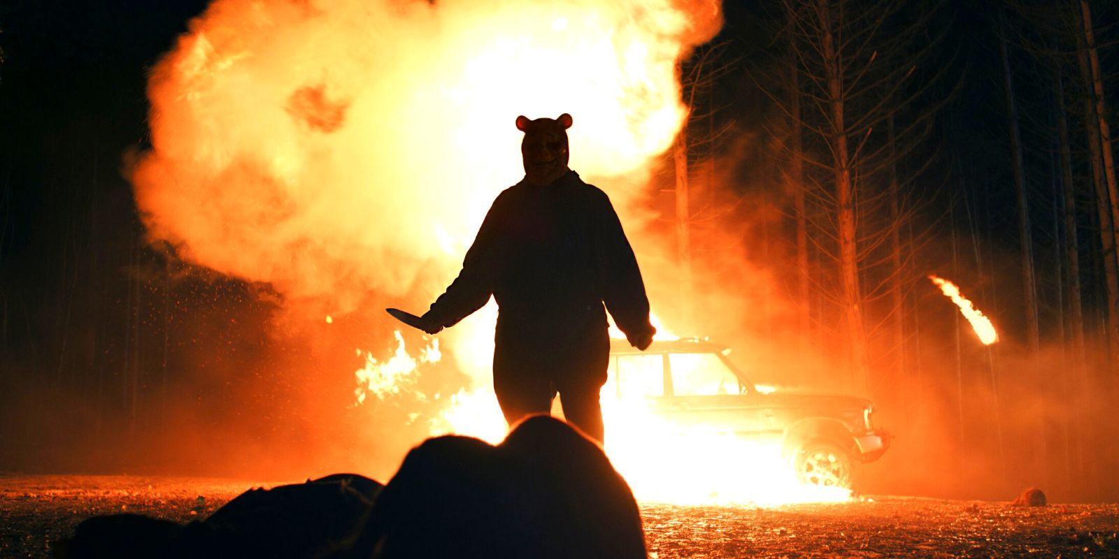 Winnie-The-Pooh posing with a knife in front of a burning car