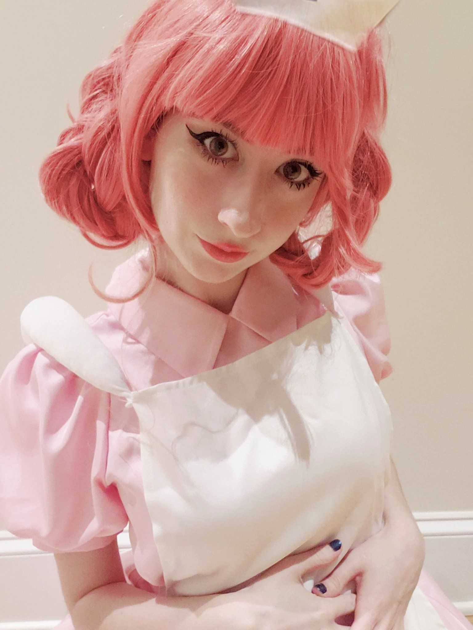 Pink-haired white woman wearing a pink and white nurse's costume in cosplay of Pokémon's Nurse Joy