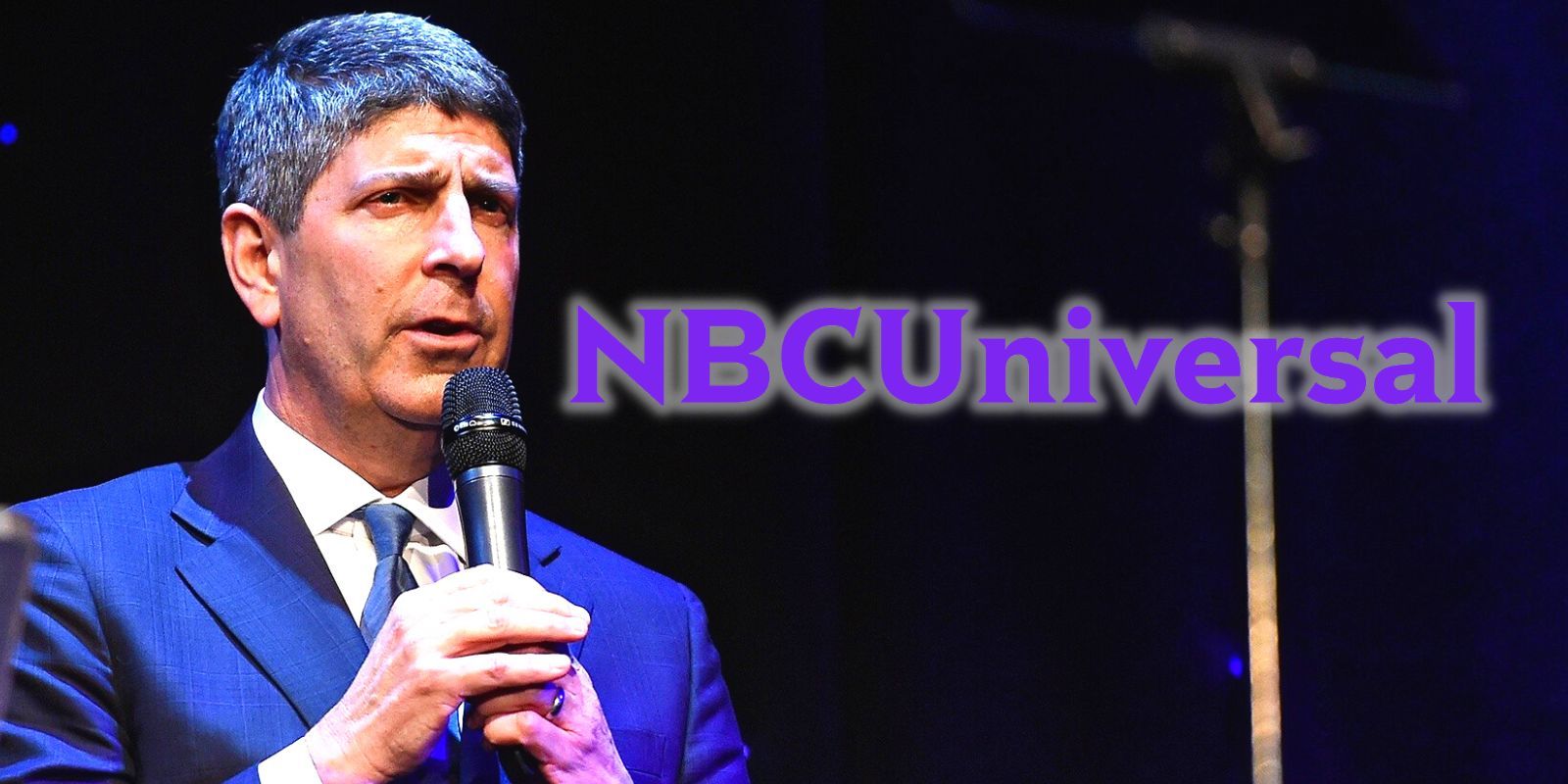 NBCUniversal CEO Jeff Shell with a microphone standing alongside the company's logo