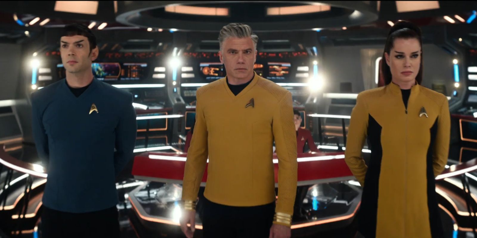 Anson Mount, Ethan Peck, and Rebecca Romijn standing aboard the bridge of the Starship Enterprise star trek strange new worlds season 2 trailer in costume as Captain Christopher Pike, Spock, and Una Chin-Riley respectively