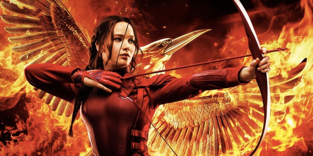 Katniss Everdeen aims her bow and arrow in front of a flaming Mockingjay